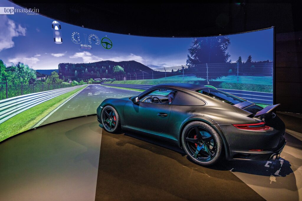 Ein Sportwagen steht im Pirelli Fahrsimulator des Virtual Development Center vor einer großen, gekrümmten Leinwand, die eine Rennstrecke simuliert.