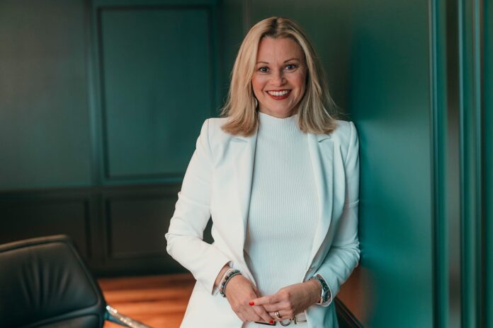 Porträt von Stefanie Brandes, COO der Dorint Hotelgruppe und neues Mitglied im IHA-Beirat, die in einem weißen Blazer vor einer grünen Wand steht.