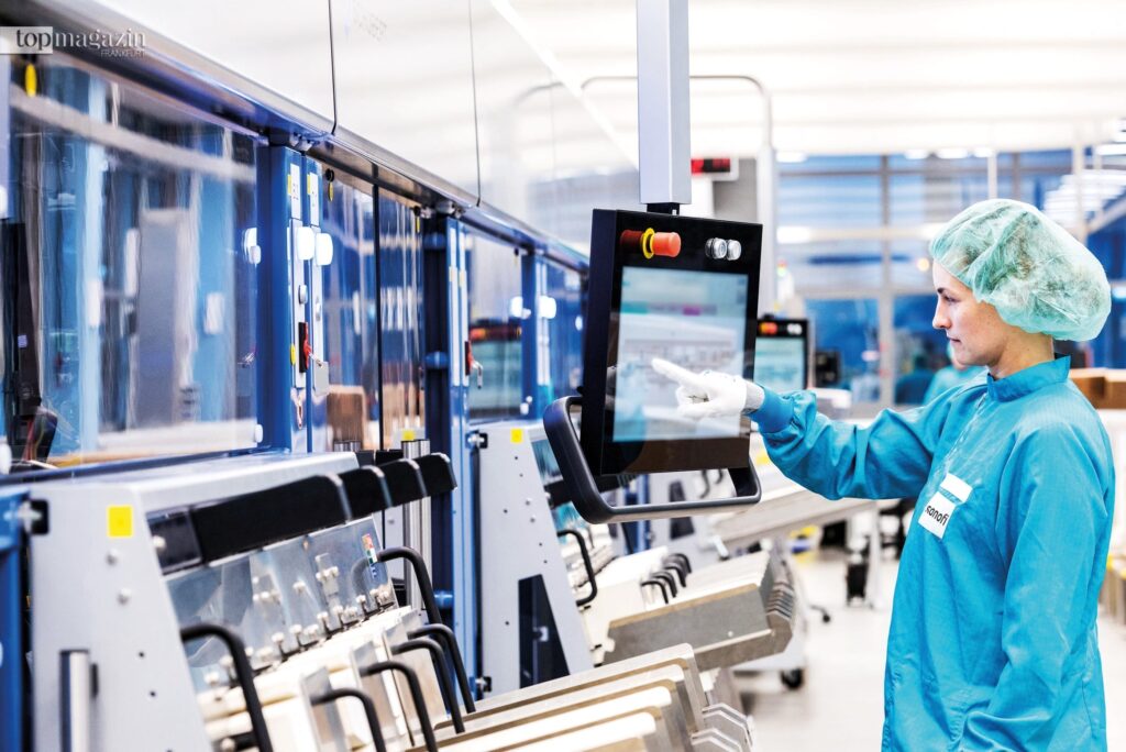 Mitarbeiterin in Schutzkleidung bedient eine hochmoderne Produktionsanlage für Insulin-Pens bei Sanofi in Frankfurt.