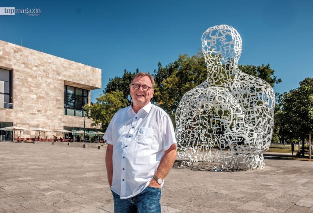 Thomas Brand, Student beim Seniorenstudium Frankfurt, steht vor der Skulptur 'Body of Knowledge' auf dem Campus Westend der Goethe-Universität.