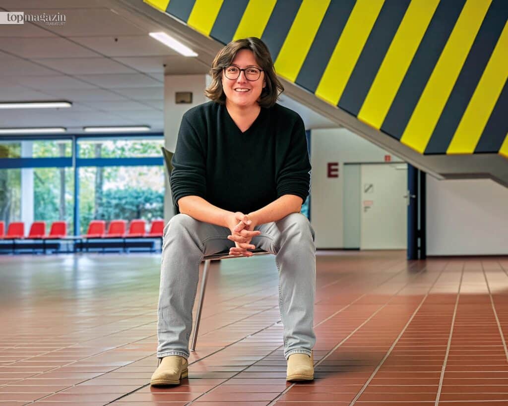 Dr. Mayte Zimmermann, Leiterin der Geschäftsstelle der Universität des 3. Lebensalters (U3L) Frankfurt, sitzt in einem modernen Universitätsgebäude.