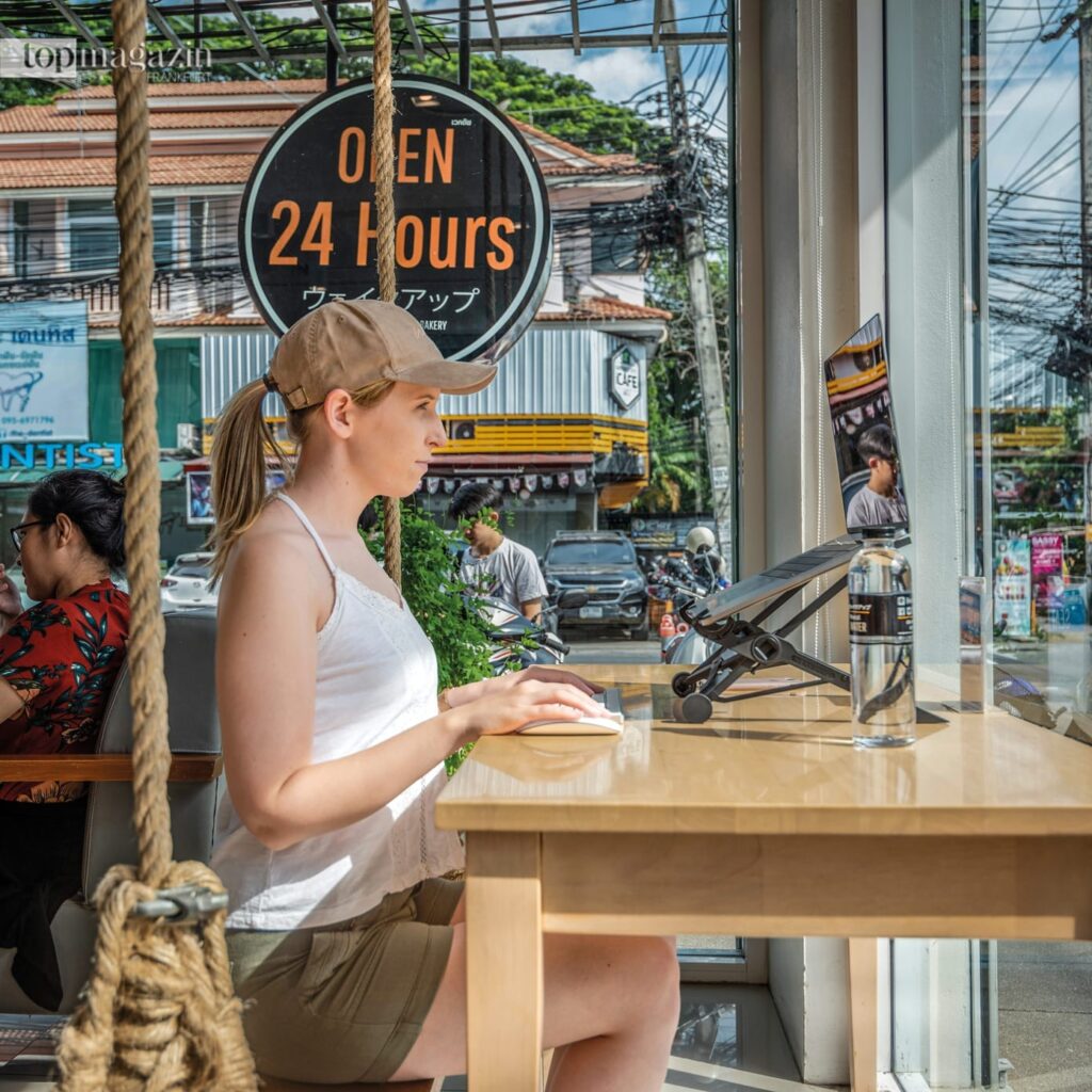 Eine junge Frau als digitale Nomadin arbeitet konzentriert an ihrem Laptop in einem modernen Café im Ausland und lebt das Modell der Workation.