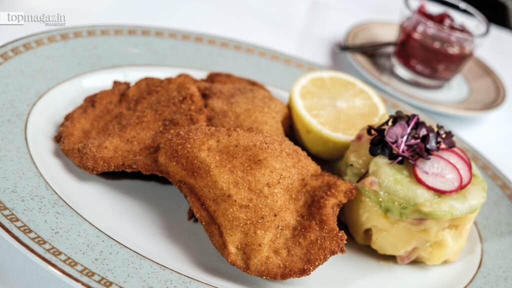 Ein klassisches Wiener Schnitzel vom Kalb, goldbraun gebacken, auf einem edlen Porzellanteller mit Kartoffelsalat und Zitrone serviert.
