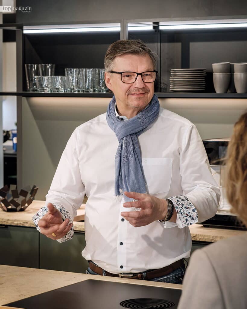 Küchenexperte Gerhard Grohs erklärt im Kundengespräch engagiert die Details einer modernen Küchenausstattung an einem Kochfeld.