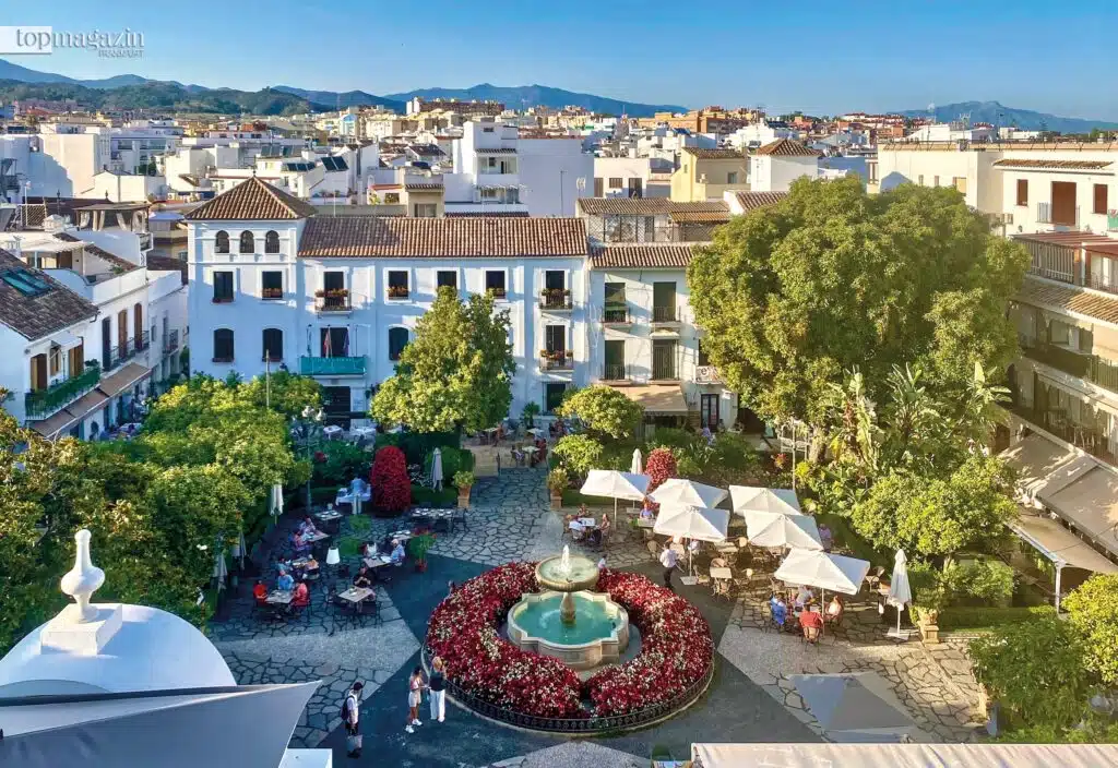 Blick von oben auf die belebte Plaza de las Flores in der Altstadt von Marbella mit Springbrunnen, bunten Blumen und weißen Häusern.