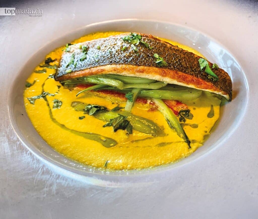 Appetitlich angerichtetes Filet vom Wolfsbarsch mit grünem Spargel und Krabbenfleisch in einer gelben Lemongrass-Kokos-Sauce auf weißem Teller.