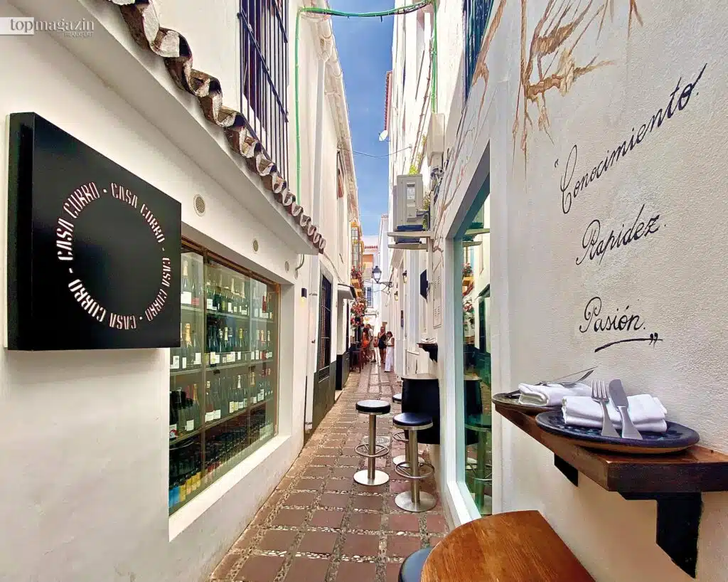 Blick in eine enge weiße Gasse in der Altstadt von Marbella mit dem runden schwarzen Schild der Taberna Casa Curro.
