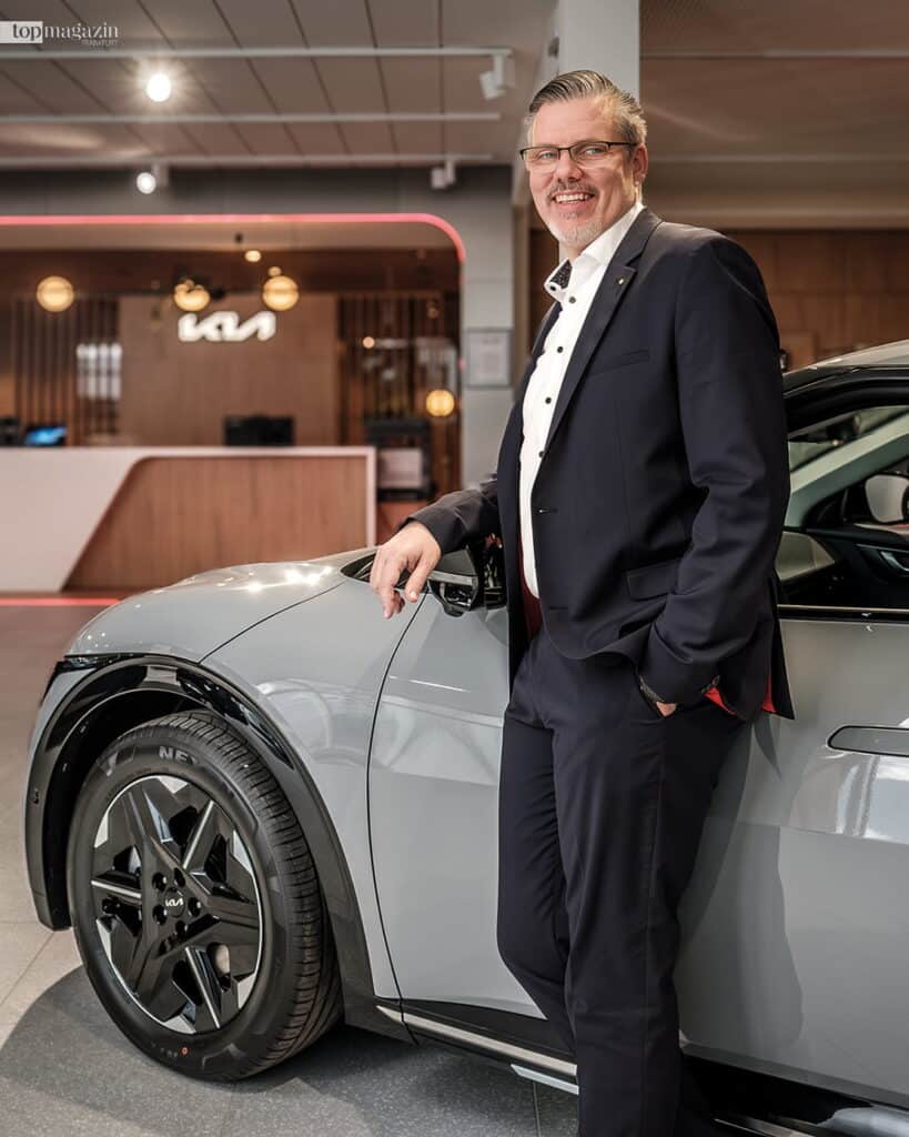 Thomas Wächter, Geschäftsführer der Hessengarage, steht lächelnd neben einem grauen Kia im Showroom.