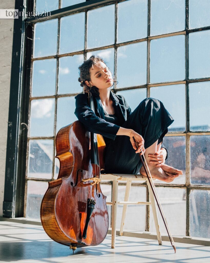 Die Cellistin Anastasia Kobekina sitzt barfuß mit ihrem Cello am Fenster eines hellen Lofts.