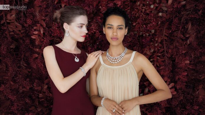 Zwei Models tragen funkelnde Diamant-Halsketten aus der Snowflake-Kollektion von Van Cleef & Arpels vor tiefrotem floralem Hintergrund.