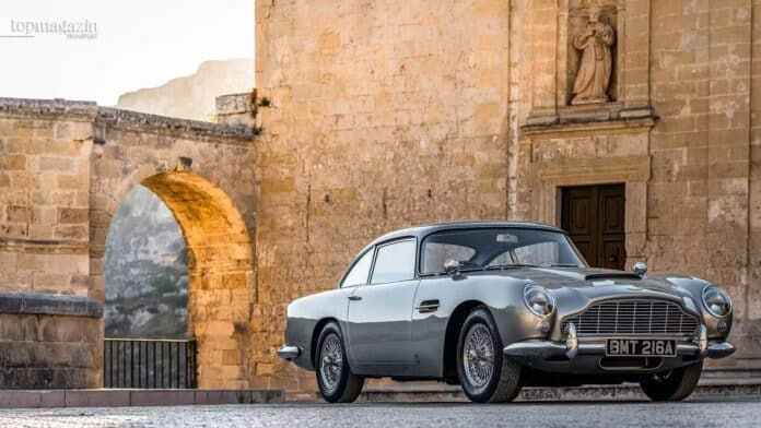 Ein klassischer silberner Aston Martin DB5 Oldtimer vor historischen Steingebäuden und einem Rundbogen in warmem Sonnenlicht als Symbol für unvergänglichen Luxus.