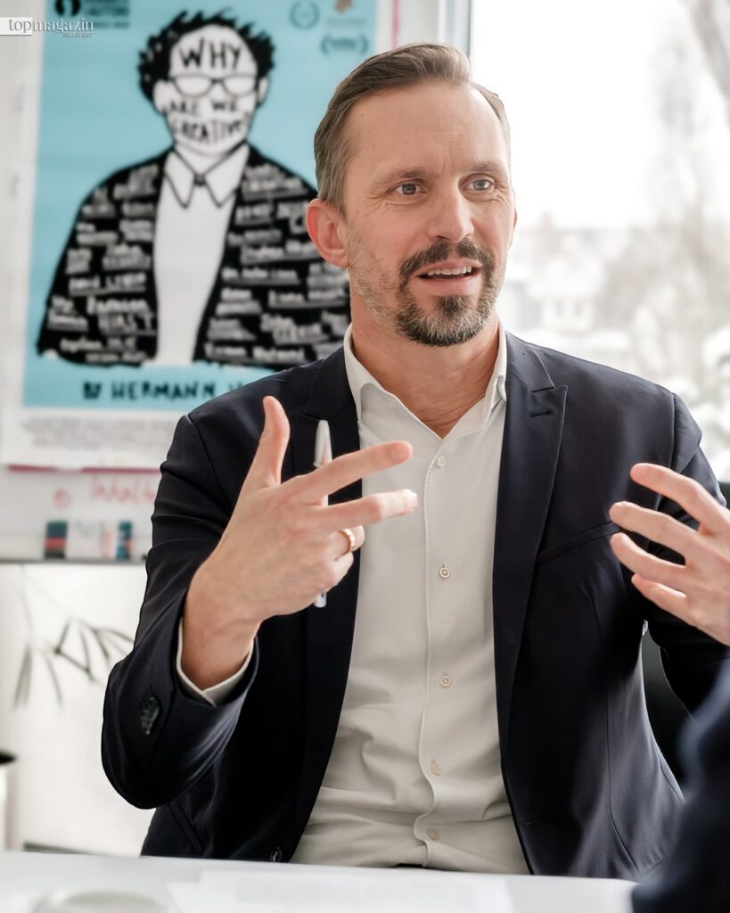 Medienmanager Florian Hager im Interview, im Hintergrund das Filmplakat Why Are We Creative