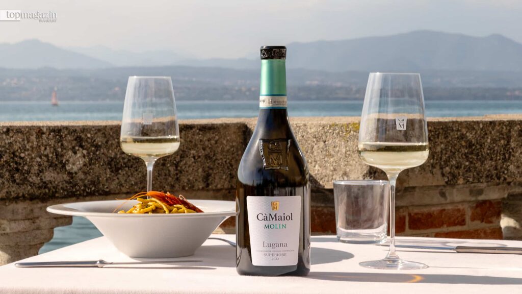 Eine Flasche Cà Maiol Lugana Superiore Wein mit zwei gefüllten Weingläsern auf einem gedeckten Tisch am Gardasee.