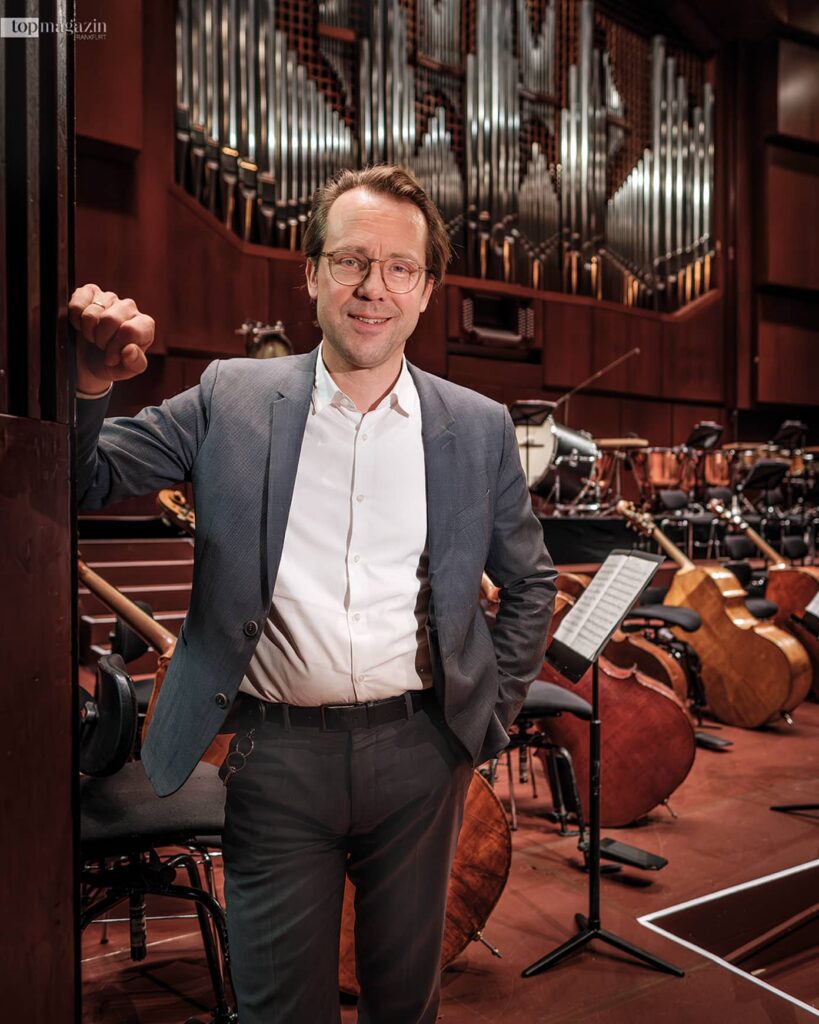 Markus Fein steht vor der Orgel im Großen Saal der Alten Oper Frankfurt zwischen Instrumenten des Orchesters