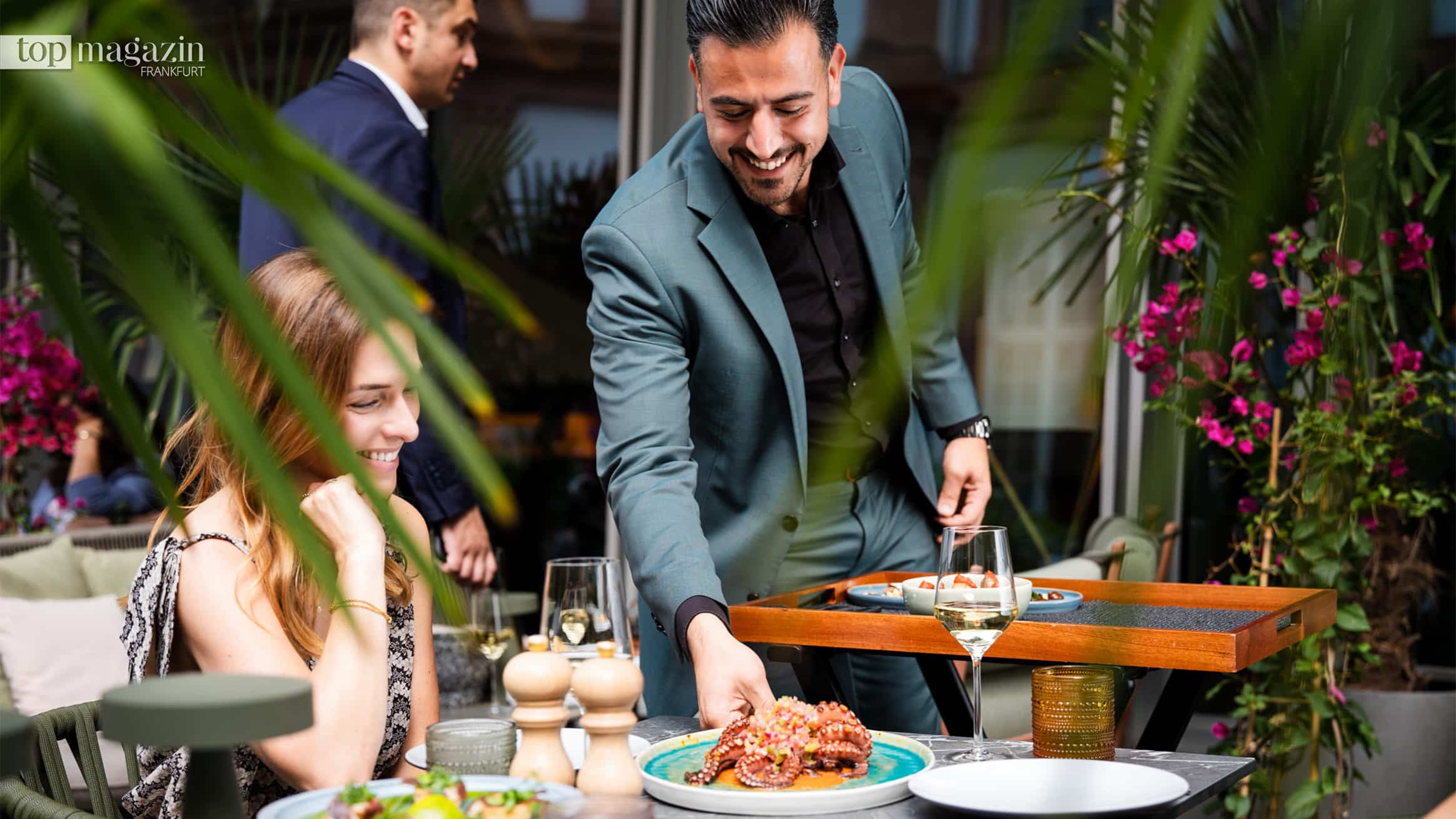 Gastgeber Ali Mohamad serviert Gästen Speisen auf der begrünten Sommerterrasse des GRETA OTO Frankfurt
