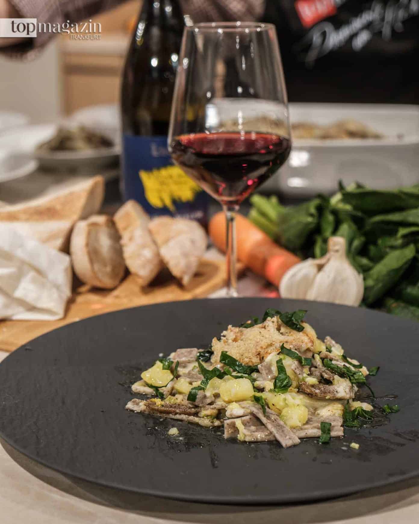 Fertig angerichteter Teller traditioneller Veltliner Pizzoccheri mit Buchweizennudeln, Wirsing, Kartoffeln, geschmolzenem Alpkäse und Rotwein im Hintergrund.