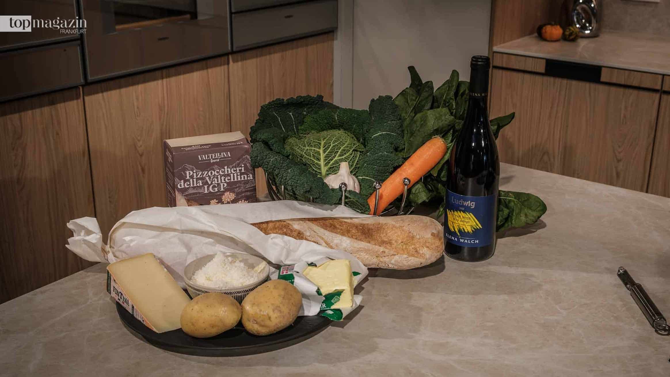 Zutaten für traditionelle Veltliner Pizzoccheri mit Buchweizennudeln, Wirsing, Kartoffeln, Alpkäse und Rotwein auf einer Küchenarbeitsplatte.