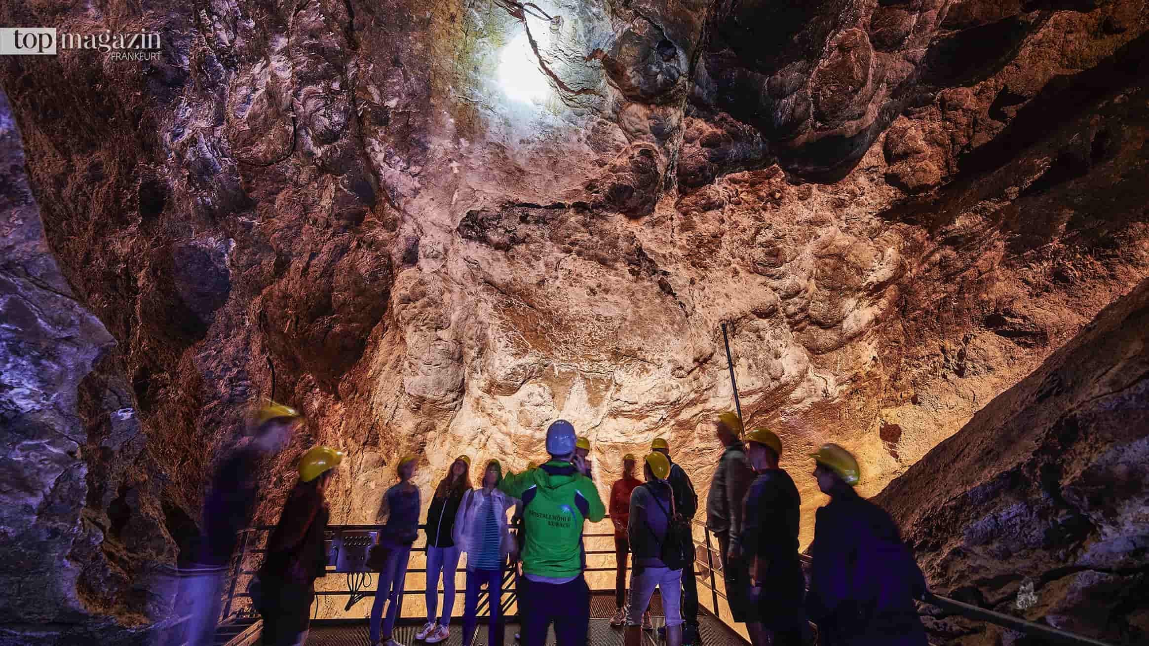 Besuchergruppe mit Helmen steht in der Halle der Kubacher Kristallhöhle unter einer hohen, kristallbesetzten Kuppel