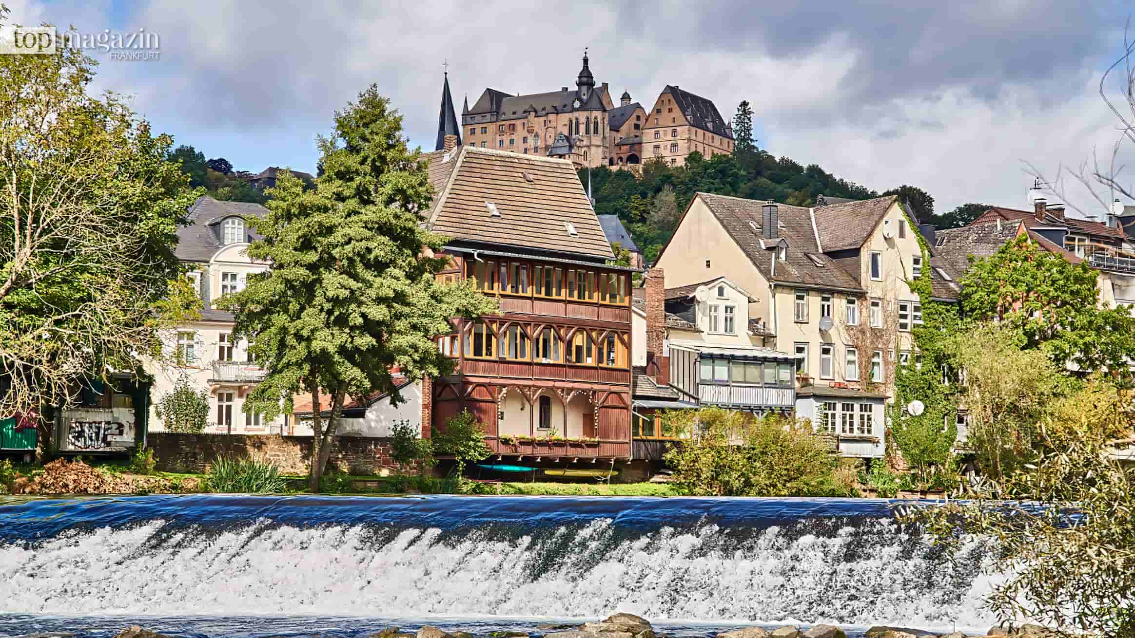 Wehr an der Lahn in Marburg, dahinter Fachwerkhäuser der Altstadt und das Landgrafenschloss auf dem Schlossberg