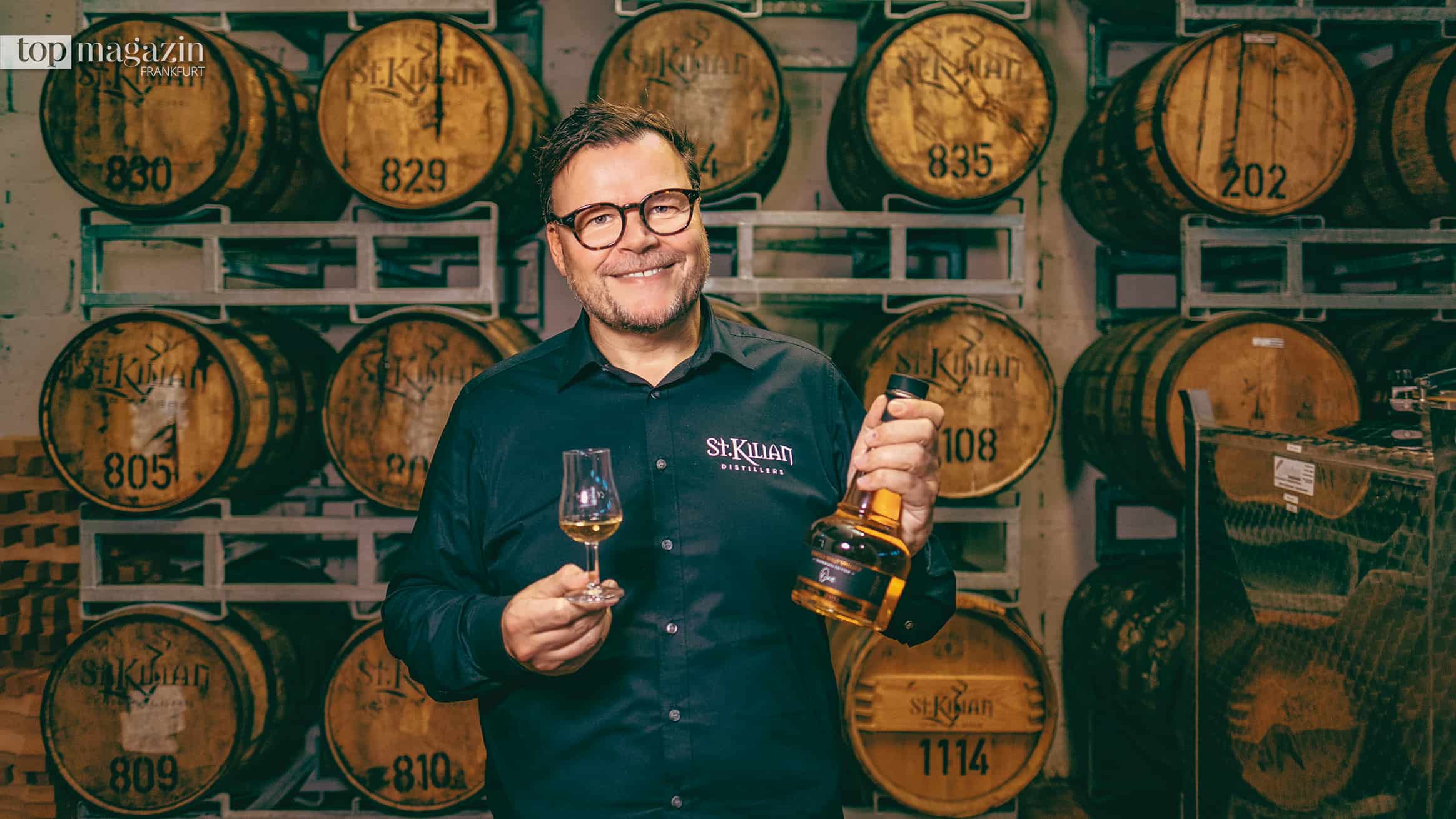 Andreas Thümmler, Gründer der St. Kilian Distillers, mit Whiskyglas und Flasche vor Fässern im Lager in Rüdenau